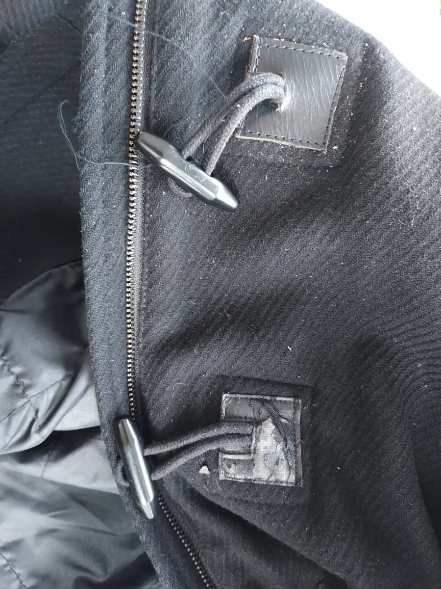Brandebourgs d'un manteau noir en laine&nbsp;: boutons bûchettes et cordons noirs fixés par des pattes en cuir